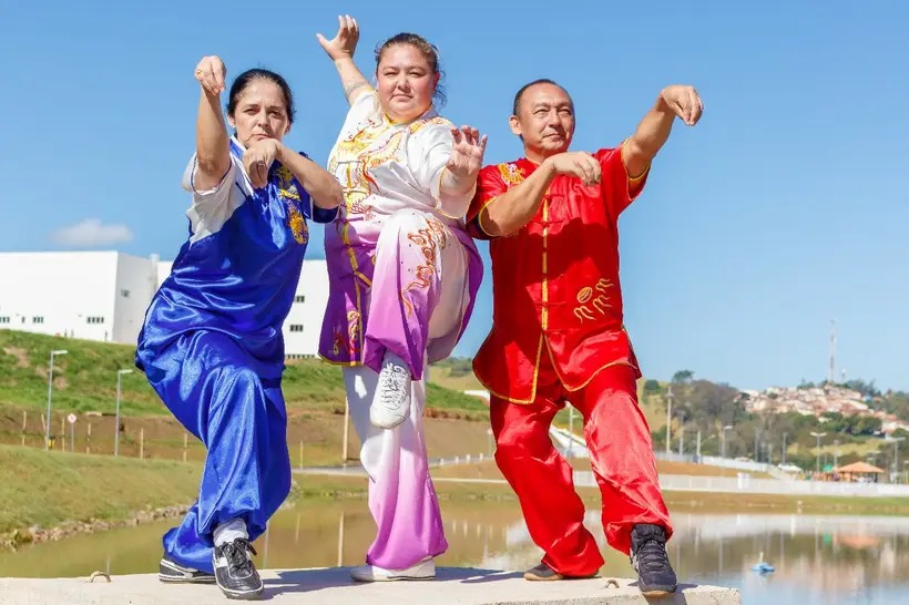 Tamiris em uniforme de artes marciais ao lado de dois mestres